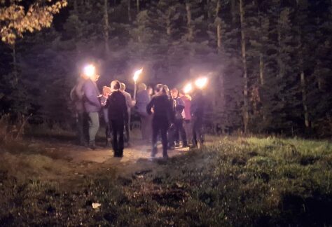 Gruppe mit brennenden Fackeln bei nächtlicher Wanderung durch den Wald in nebligem Ambiente